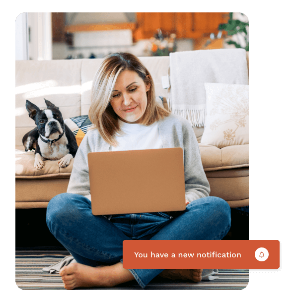 Woman sitting on the floor with her laptop checking a notification while a dog sits behind her on a couch